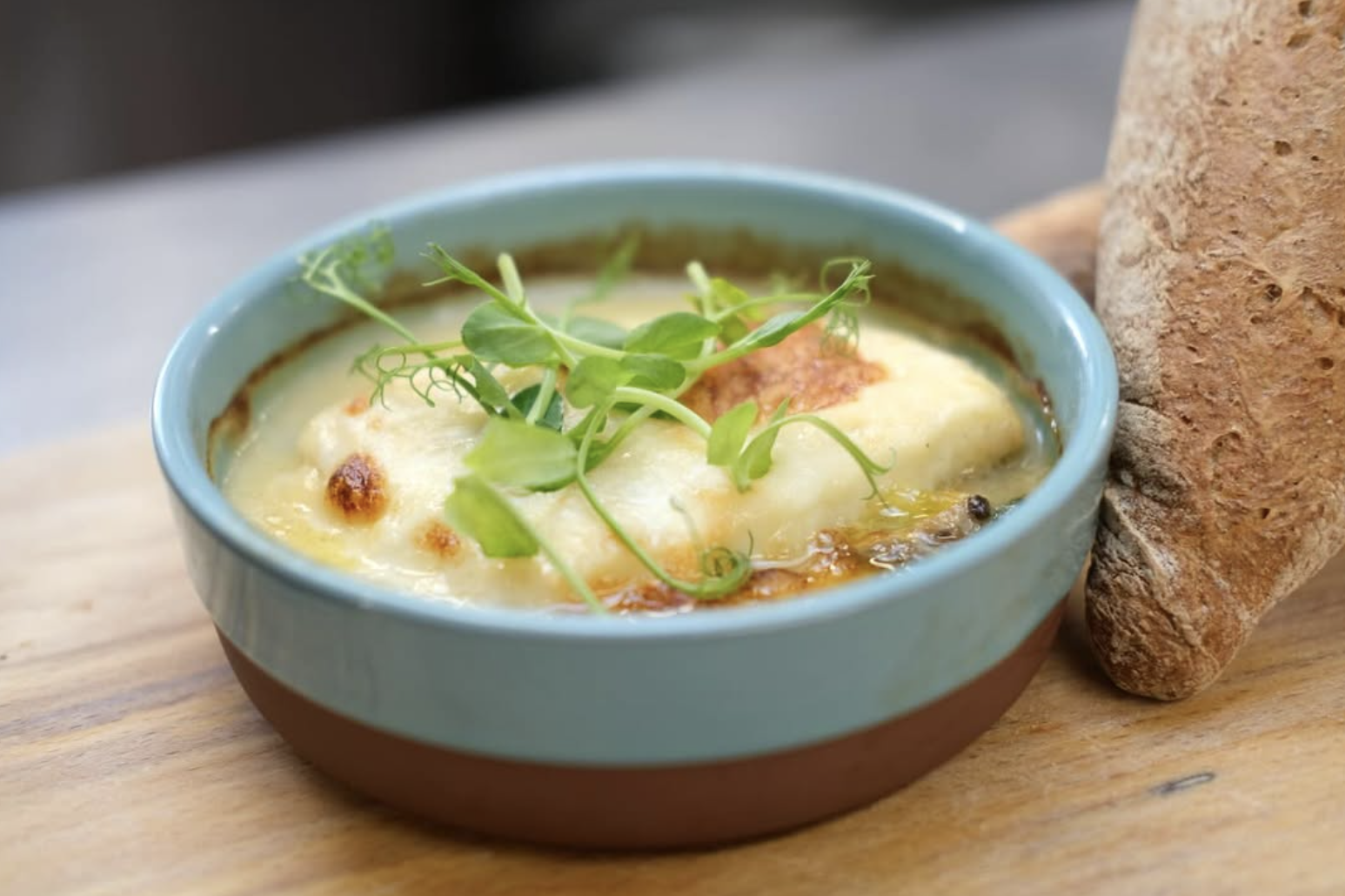 Baked dish with golden cheese topping and pea shoots, served with crusty bread